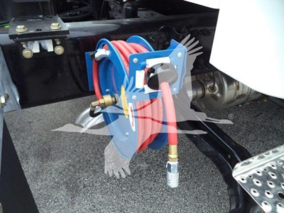 Coiled red air hose on a blue reel mounted to Freightliner M2 106 chassis, with metallic fittings and hose connected to a port near the frame