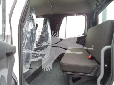 Cab interior of a Freightliner M2 106 rollback truck showing front passenger seat and rear seating area with plastic-covered seats and window light.
