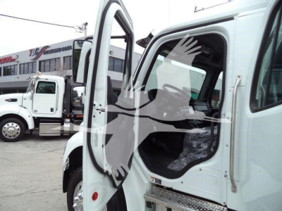 Truck cabin door open showing Freightliner M2 106 cab interior and chrome step, side mirror, and window from a rollback truck in a dealership lot.
