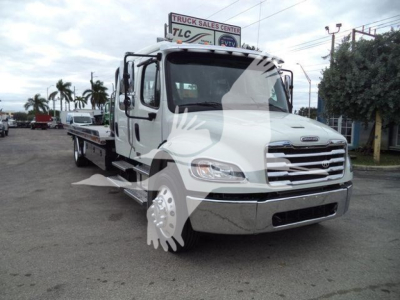 Freightliner M2 106 rollback truck in a lot, white cab with chrome bumper, extended side steps, and flatbed.