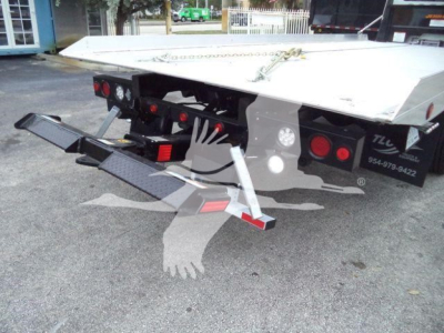 Trailer hitch and rear of a flatbed rollback tow truck showing loading ramps and taillights.
