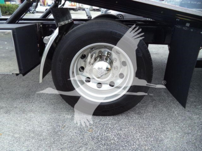 Freightliner M2 106 wheel and front suspension area showing steel alloy wheel and tire under trailer frame; mudflap and chassis components visible.