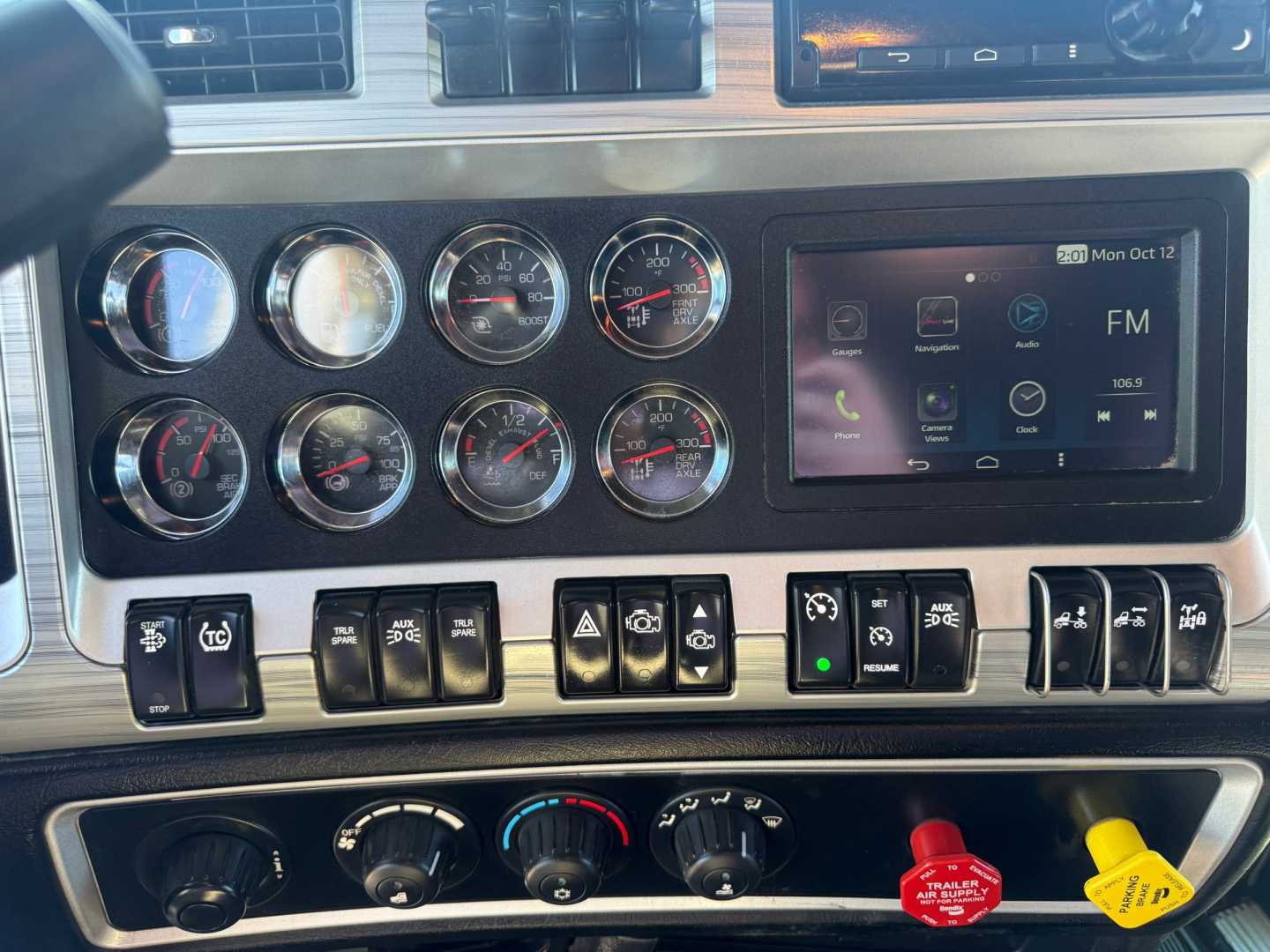 Kenworth W900L dashboard and control switches showing multiple gauges and an infotainment screen.