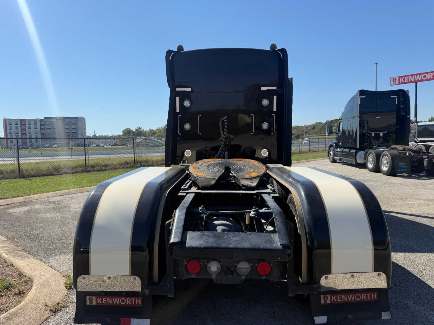 Kenworth W900L rear view showing tandem axle area, black fenders with white stripes, bumper lights, and rear chassis details.
