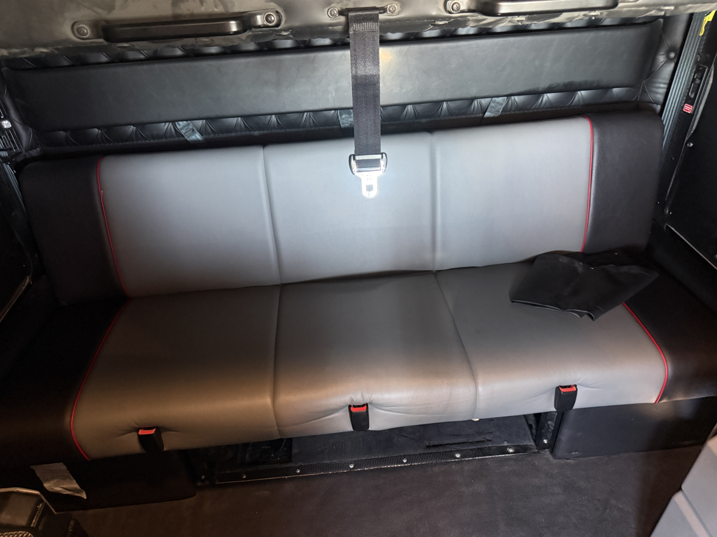 Kenworth W900L cab interior showing rear sleeper seat with grey upholstery and red piping, center seat belt strap visible.