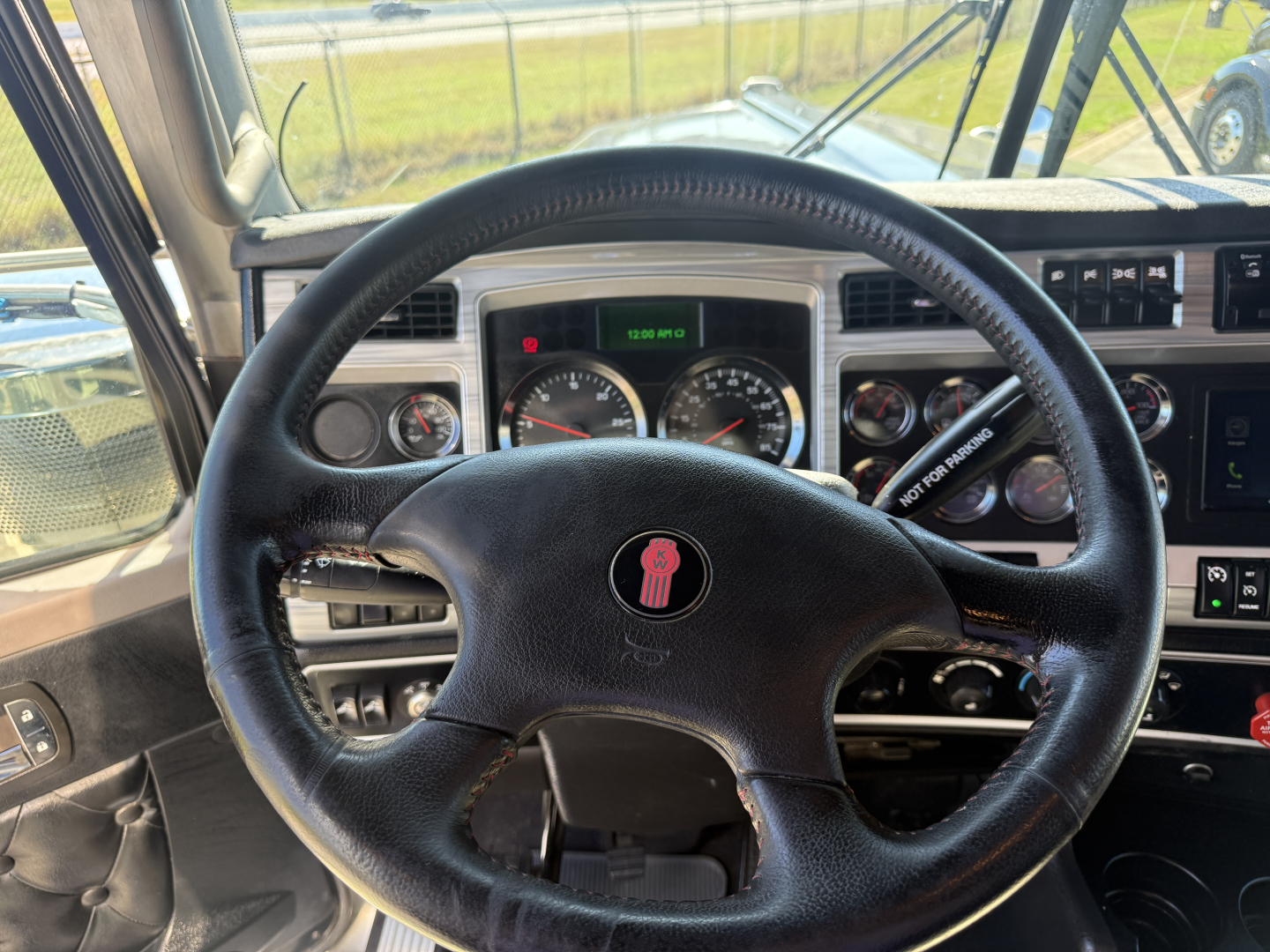 Kenworth W900L steering wheel and dashboard view with gauges and controls in the cab. Visible text includes VIN/stock data in listing, and instrument panel labels.