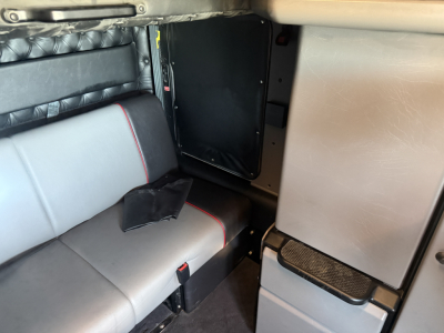 Kenworth W900L cab interior showing sleeper seat and door panel with storage, gray upholstery with red stitching, and step area.