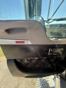 Kenworth W900L truck interior door panel with Kenworth badge and tufted black armrest leather, driver-side view.