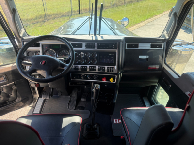 Kenworth W900L truck interior showing steering wheel, dashboard gauges, gear shift, and controls.