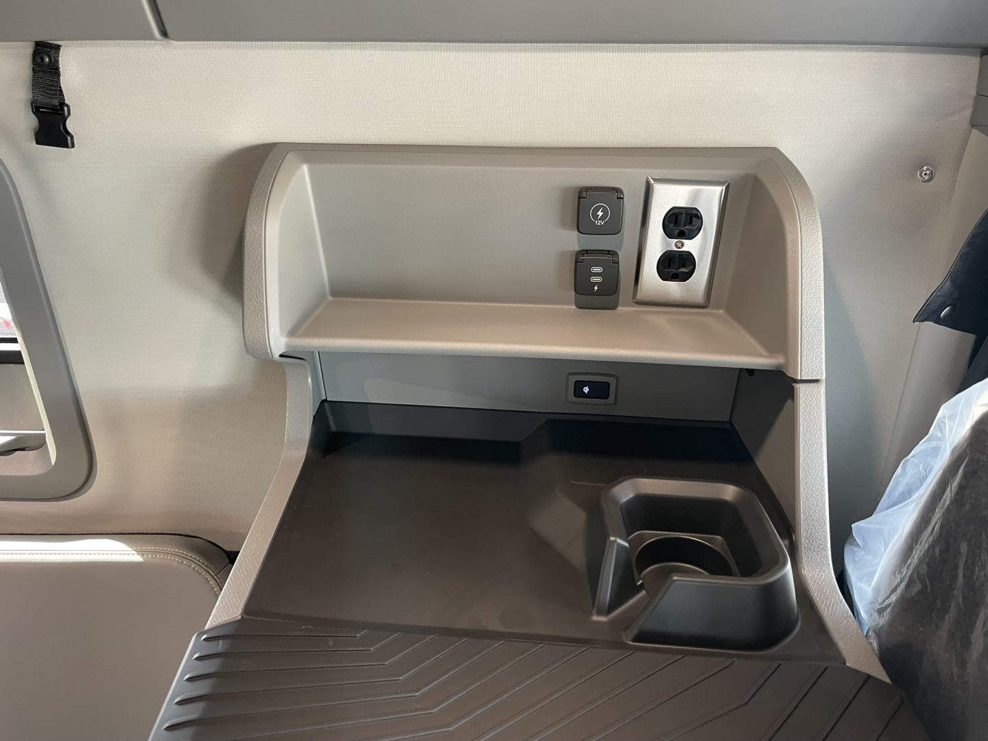 Cab area in a Volvo VNL truck showing power outlet panel and storage tray with cup holder.