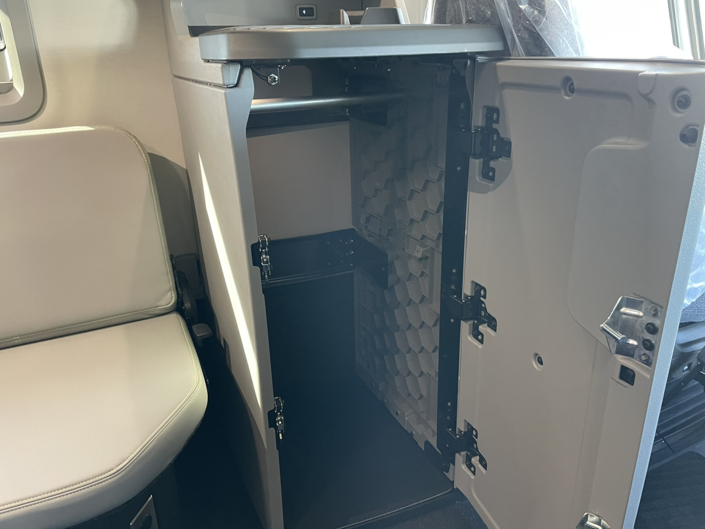 Interior storage compartment with open door under the dashboard of a 2026 Volvo VNL64T860 sleeper cab showing a small fridge-like unit and foam-lined side panel.