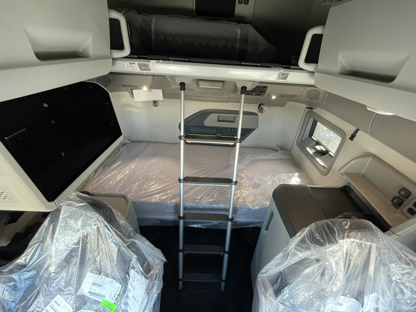 Volvo VNL64T860 tractor cab sleeper bunk area with a fold-down ladder, plastic-wrapped seats, and overhead storage panels.