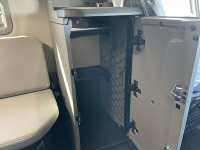 Interior storage compartment with open door under the dashboard of a 2026 Volvo VNL64T860 sleeper cab showing a small fridge-like unit and foam-lined side panel.