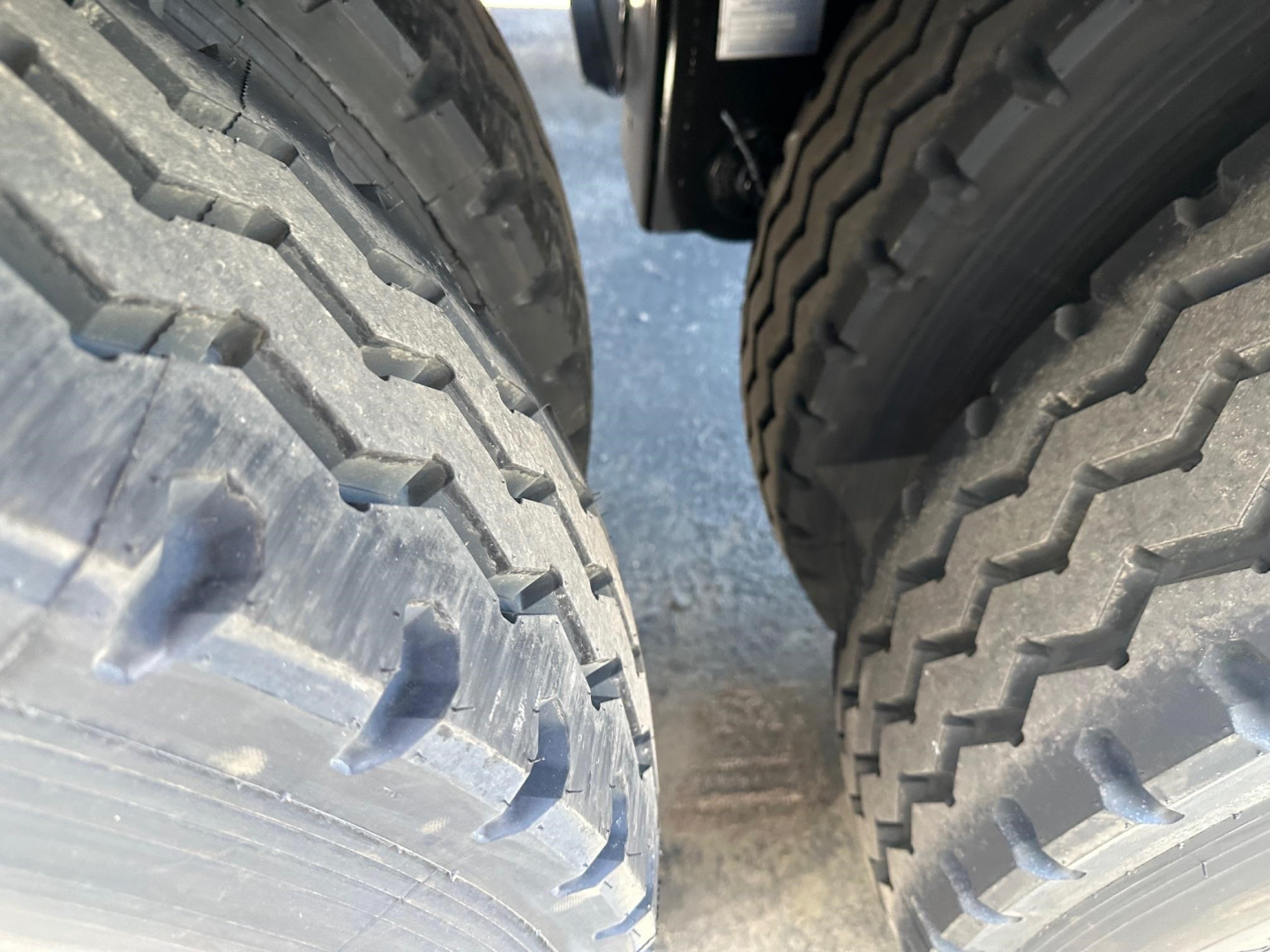 Dual large truck tires with tread pattern visible on both sides of a trailer, close-up shot showing gap between wheels.