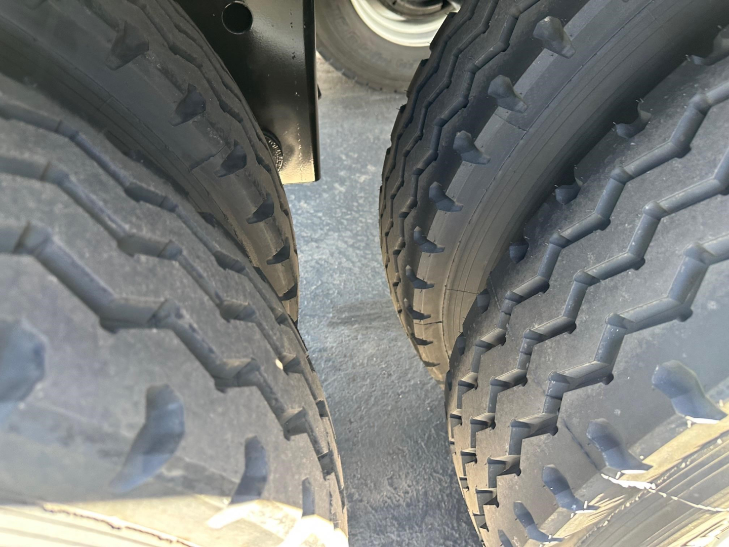 Trailer axles and dual tires of a Smithco air ride side dump unit, view between the tires showing tire treads and frame), no text visible on components.