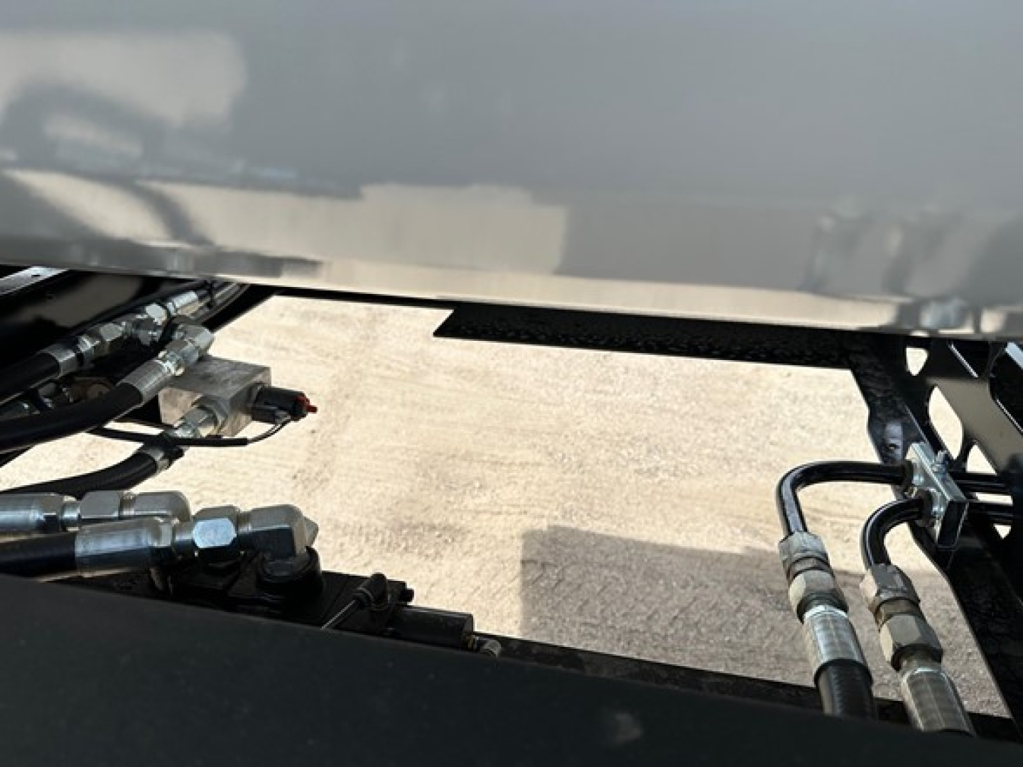 Trailer hydraulic lines and control area of 2026 Smithco Air Ride Side Dump showing hydraulic hoses and fittings under the trailer bed.