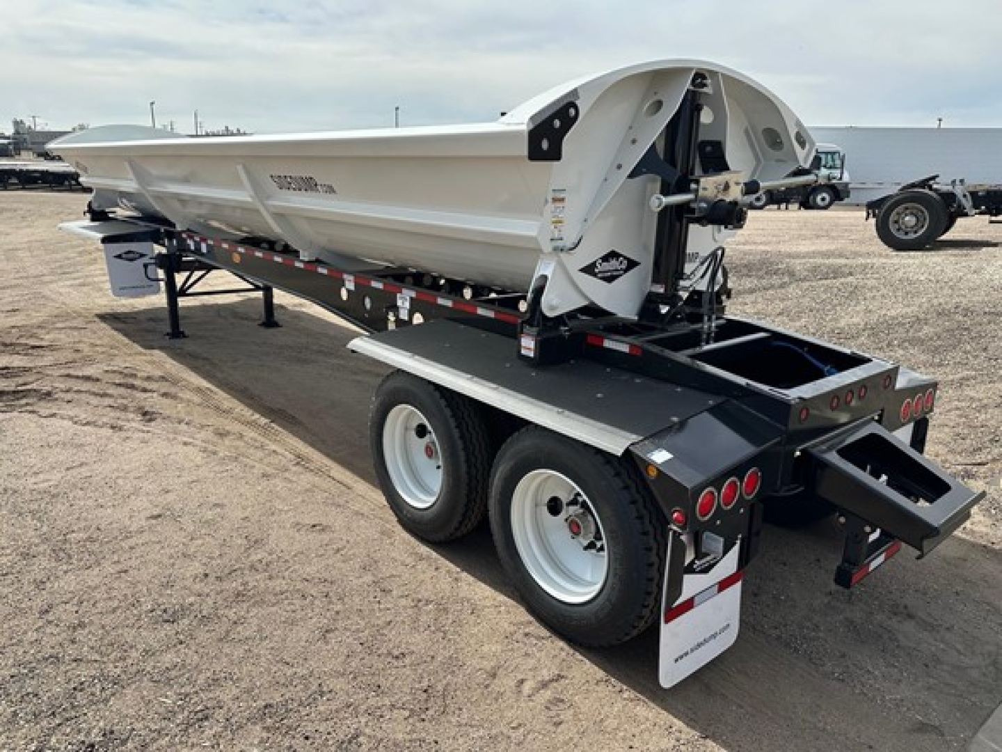 Smithco air ride side dump trailer on dual-axle trailer chassis, with hydraulic mechanisms and side panels, showing rear lights and mud flaps.