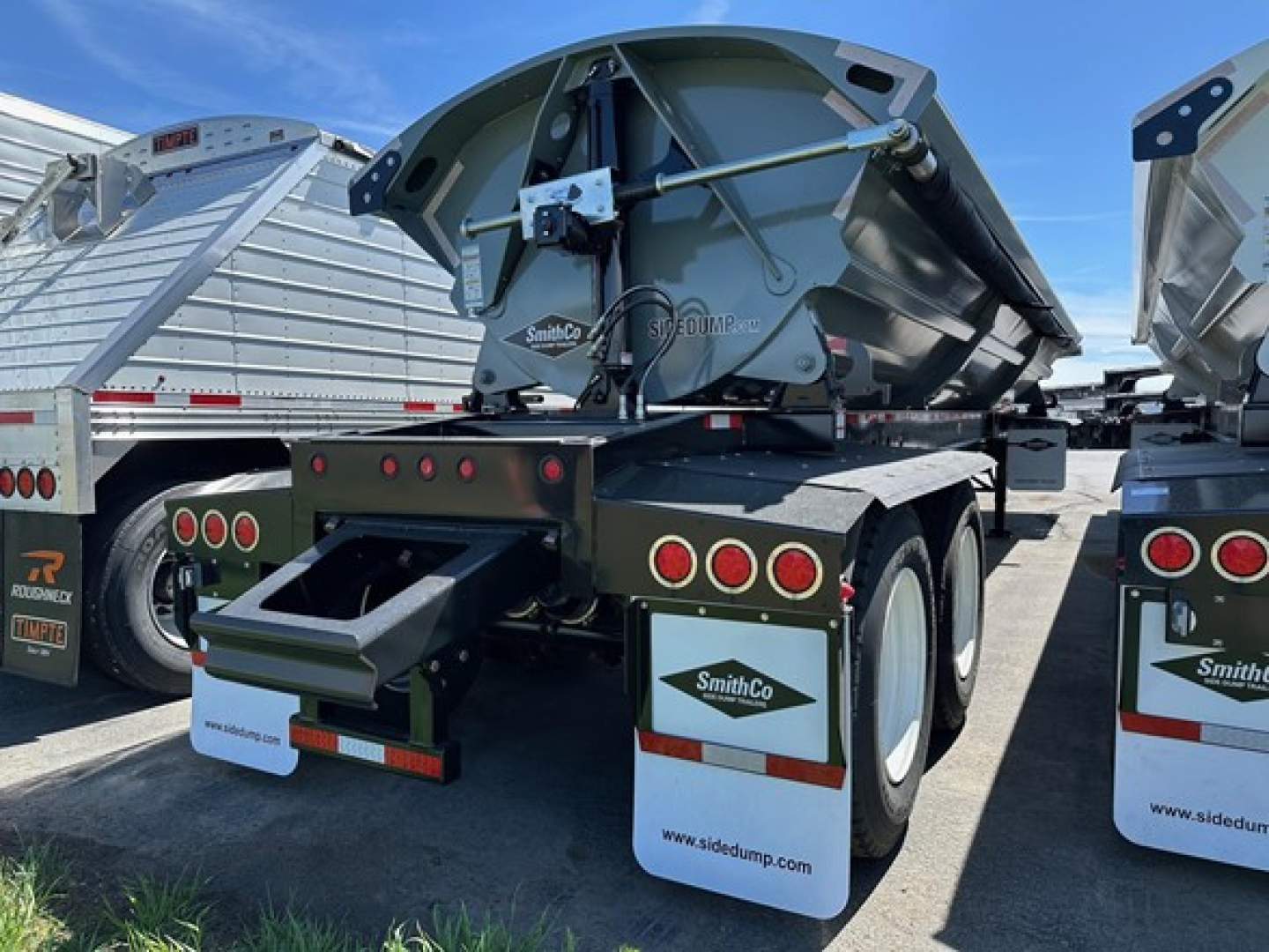 Smithco Air Ride Side Dump trailer rear view showing dual axles, taillights, mud flaps with SmithCo logo, and side dump mechanism in green/gray finish.
