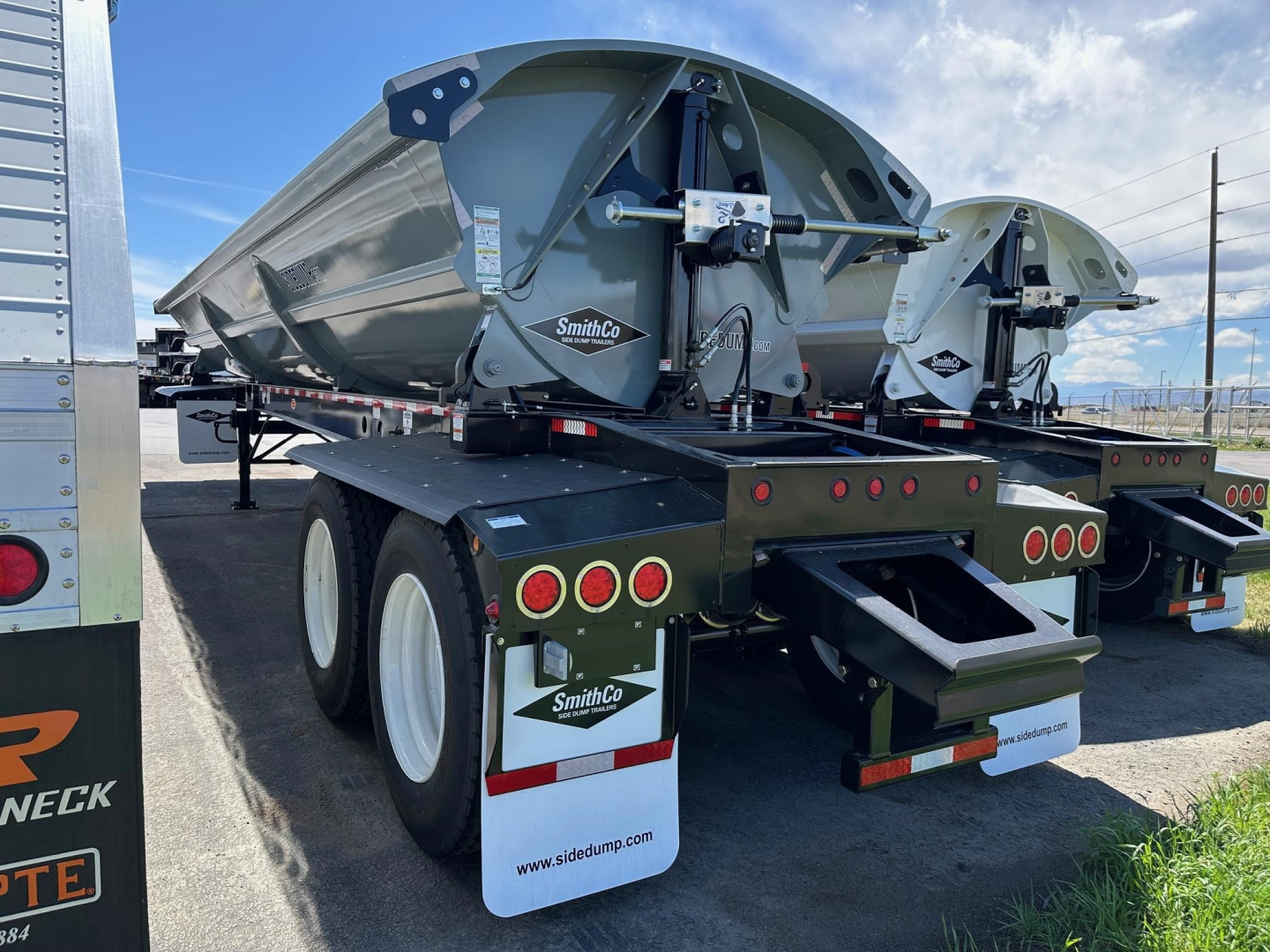 SmithCo air ride side dump trailer seen from rear-left, with dual axles and mud flaps bearing SmithCo logo; green chassis, hydraulic cylinder, and rear underride structure.