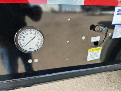 Dial gauge showing pressure reading on black trailer side with warning labels and small valve