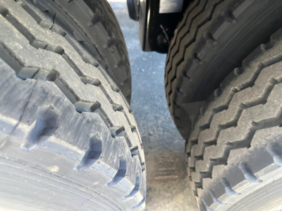 Truck trailer dual rear tires view showing heavy tread and gap between tires with mud and road grime.