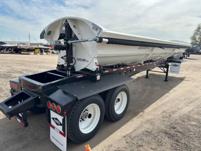 Side-dump trailer with white bed and black chassis, dual-axle rear view showing hydraulic mechanism and logo on side.
