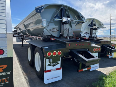 Dump trailer with SmithCo air ride side dump system, rear view showing dual axles, taillights, and white mud flaps with SmithCo logos.