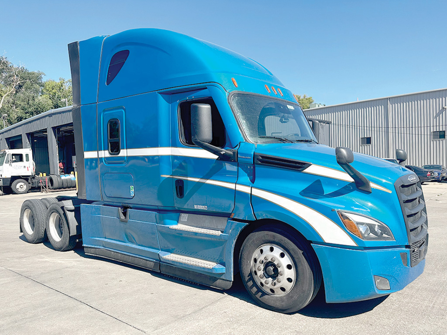 Freightliner Cascadia126 sleeper cab truck in blue with white racing stripe, side view showing front wheel and cabin, no visible text.