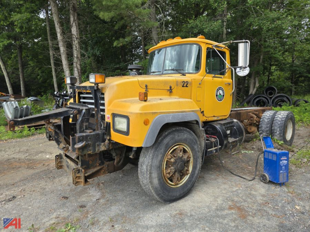 2004 Mack RD690P cab and chassis in yellow with front plow frame and heavy-duty tires, side mirrors, and a green park emblem on door.