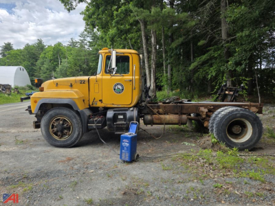 2004 Mack RD690P cab and chassis truck with yellow cab and exposed chassis, parked on gravel with a blue fluid canister nearby.