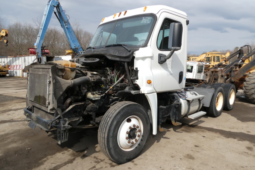 Front-left view of a damaged white Freightliner Cascadia 125 tractor with exposed engine and radiator, no sleeper cab, on a salvage lot.