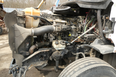 Front engine bay of a Freightliner Cascadia 125 with exposed components, hoses, and wiring; radiator, coolant reservoir, and various engine parts visible.