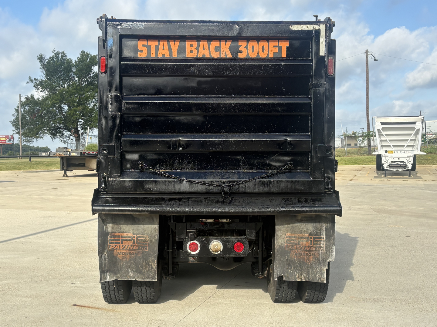 Dump truck rear showing 'STAY BACK 300FT' warning on the tailgate, Mack GR64F style with dual rear axles and mud flaps.