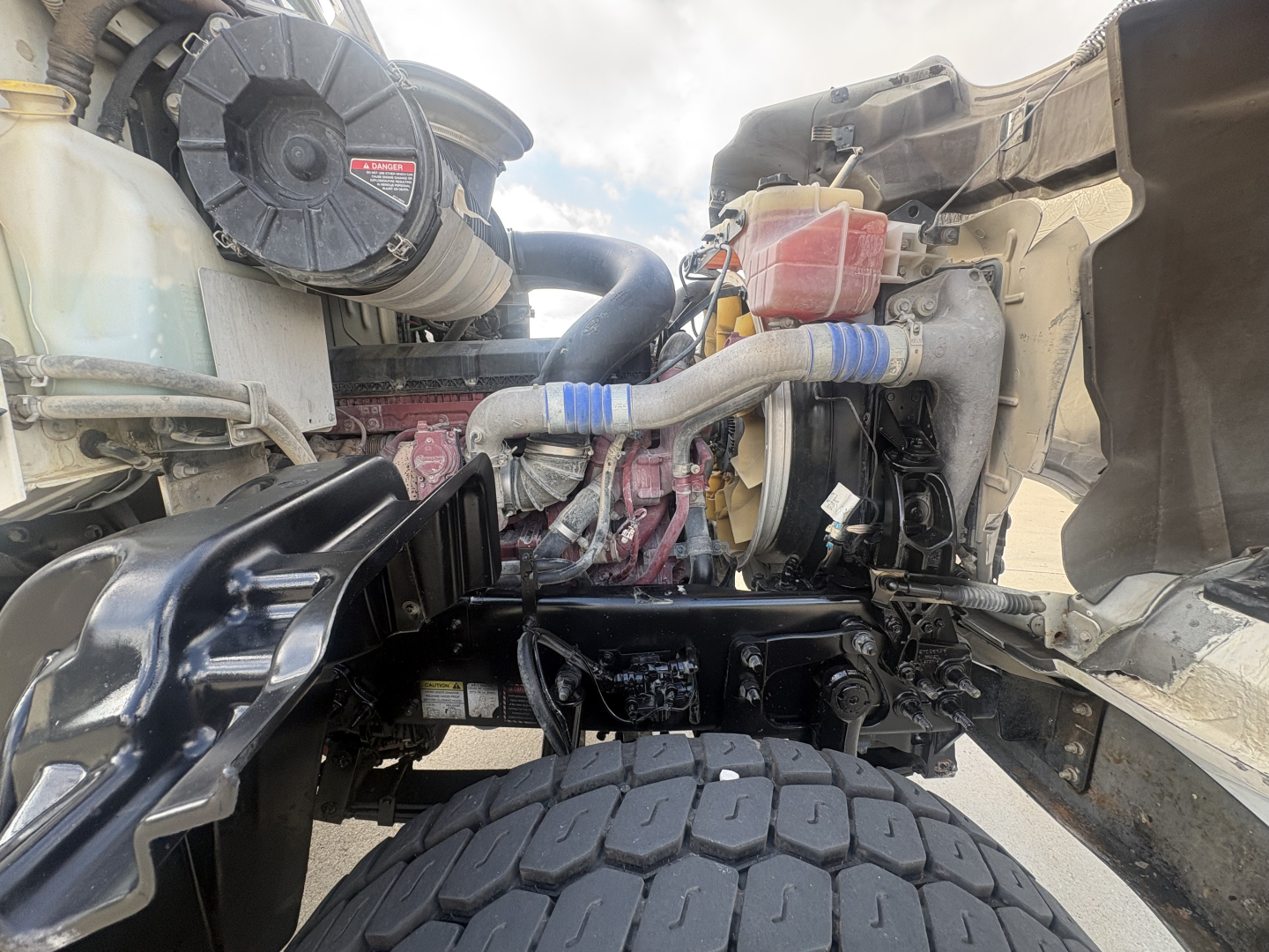 Mack GR64F truck engine bay showing coolant reservoir, hoses, and air intake with visible components.