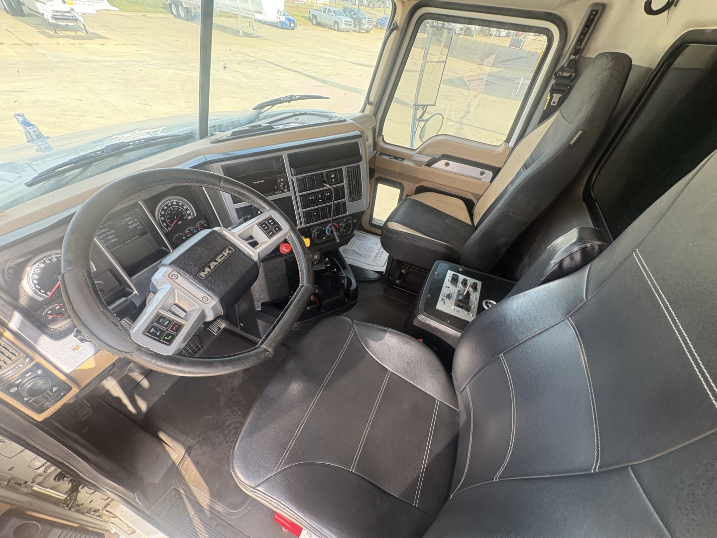 Mack GR64F truck cab interior showing steering wheel, dashboard, and driver seat with controls and passenger seat.
