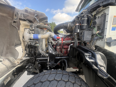 Truck engine bay of a 2022 Mack GR64F dump truck showing engine components, hoses, and intake piping from the side view.