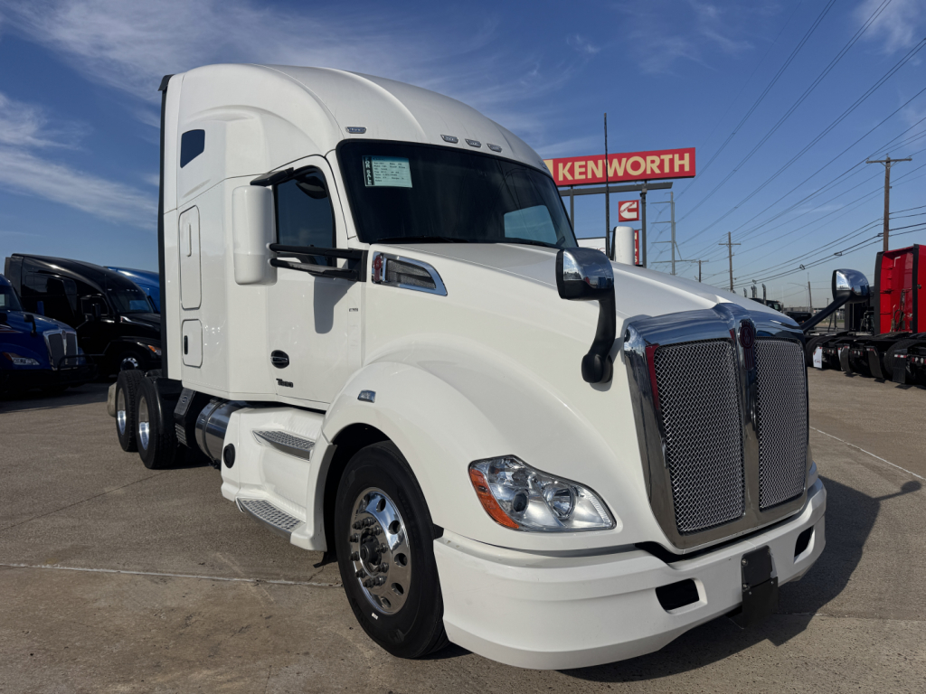 Kenworth T680 cab and front end with grille, headlights, and side mirror visible; white exterior, truck in a dealership lot.