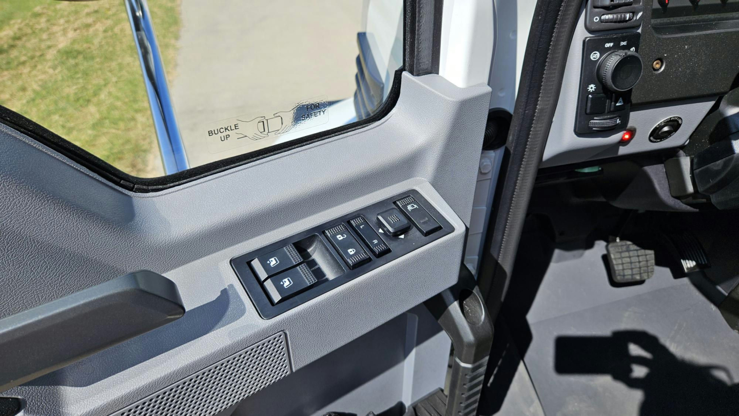 Vehicle cabin interior showing window controls on the driver's door and part of the dashboard in a Mack MD6 truck.