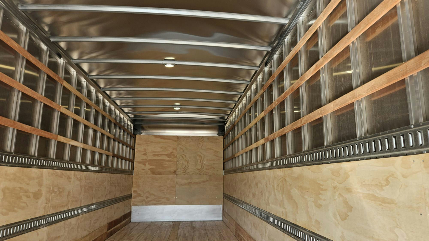 Truck trailer interior showing empty cargo area with wooden side rails and metal studs, finished plywood floor and metal ceiling beams.
