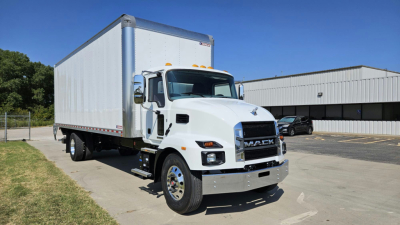 2025 Mack MD6 box truck with white cab and large white cargo box, front chrome grille, dual rear wheels, in lot near warehouse.