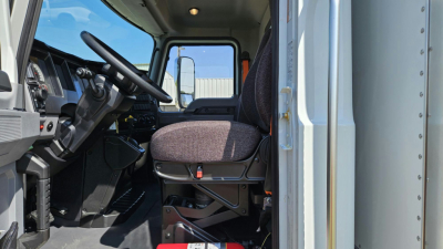 Truck cab interior of a 2025 Mack MD6 showing driver seat, steering wheel, dashboard, and entry door.