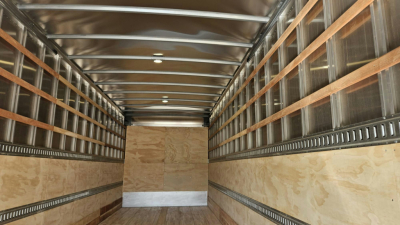 Truck trailer interior showing empty cargo area with wooden side rails and metal studs, finished plywood floor and metal ceiling beams.