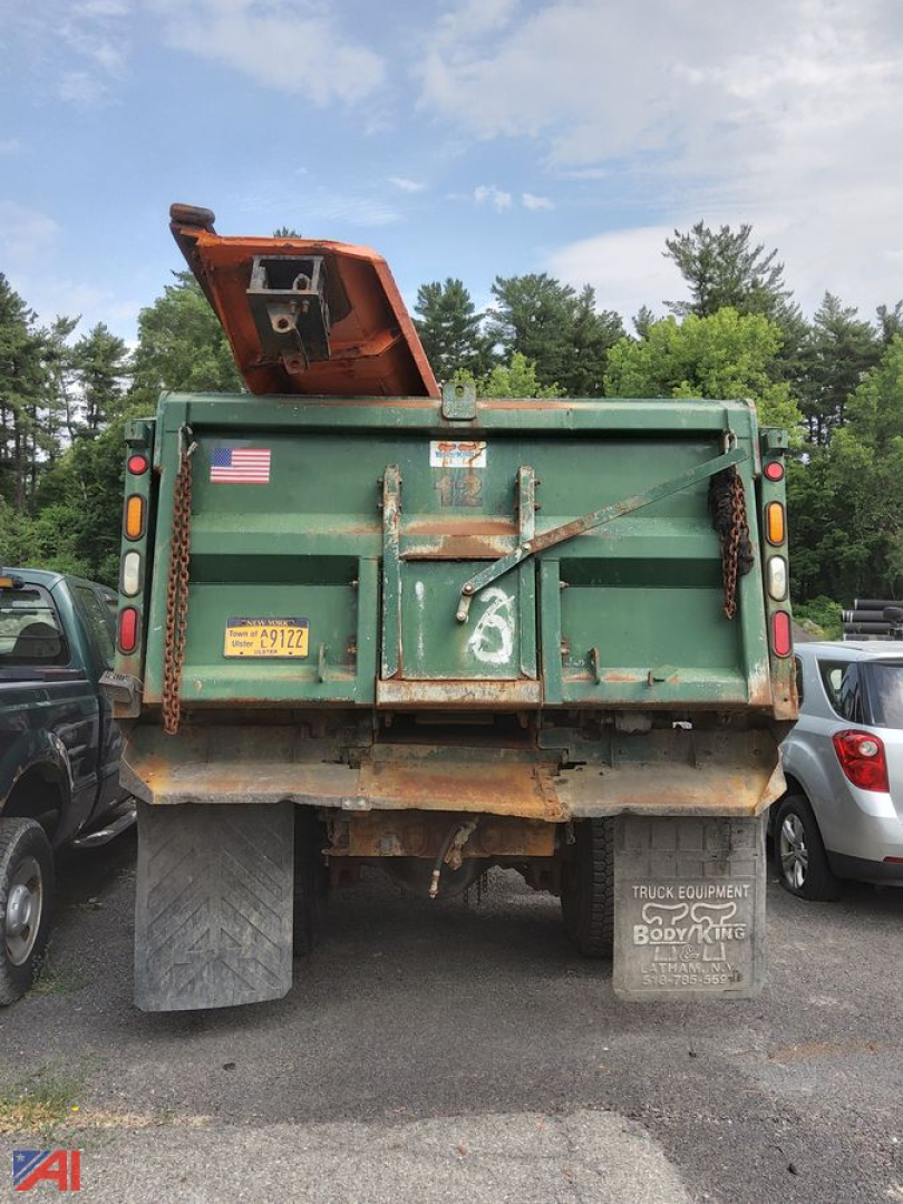 Dump truck rear showing open tailgate and plow mount with state plate and license tag.