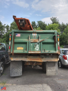Dump truck rear showing open tailgate and plow mount with state plate and license tag.