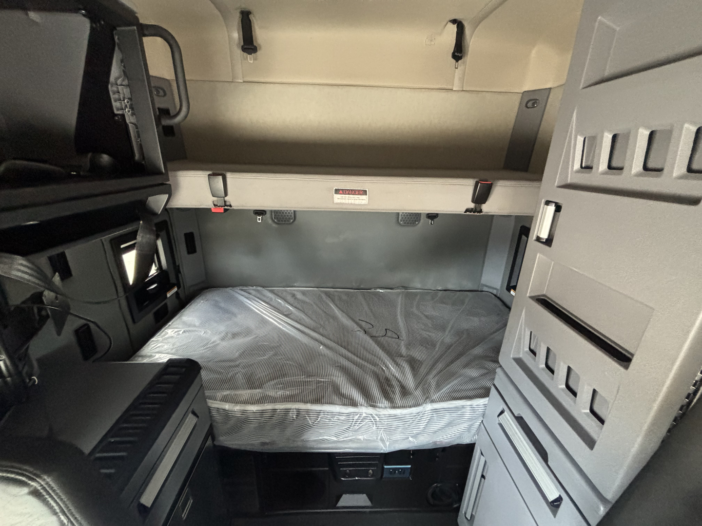 Interior sleeper cab of a 2023 Mack AN64T70 showing bed with plastic cover and storage compartments.