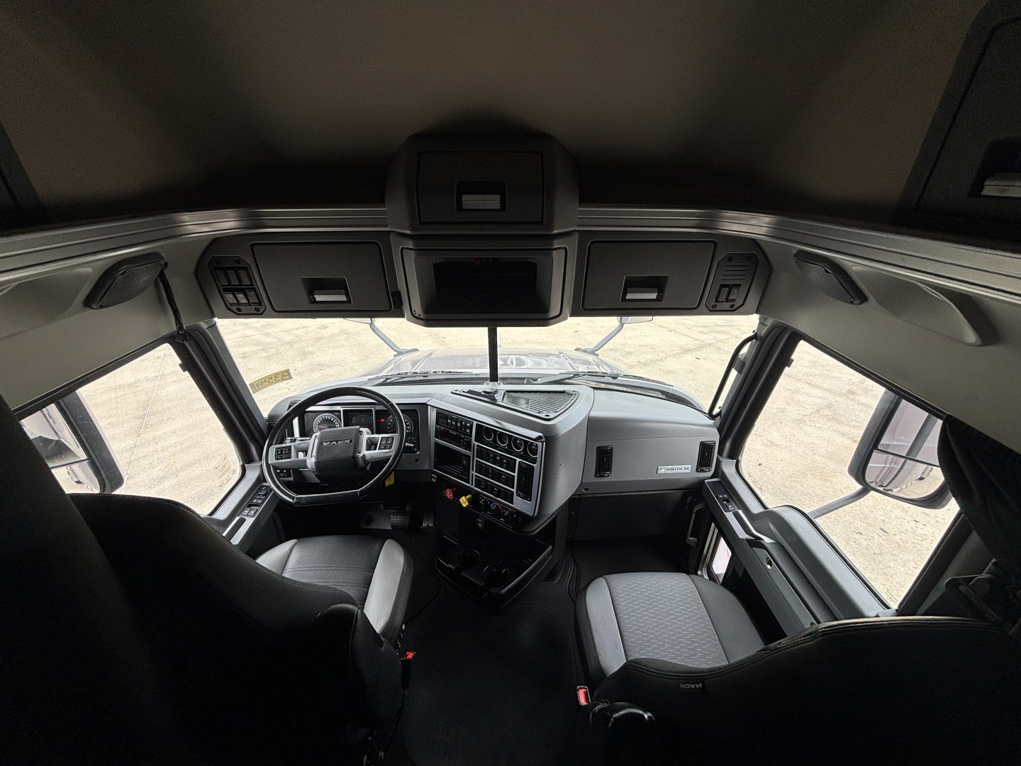 Cab interior of a 2023 Mack AN64T70 with two front seats, dashboard, steering wheel, and overhead console; visible windshield and side windows.