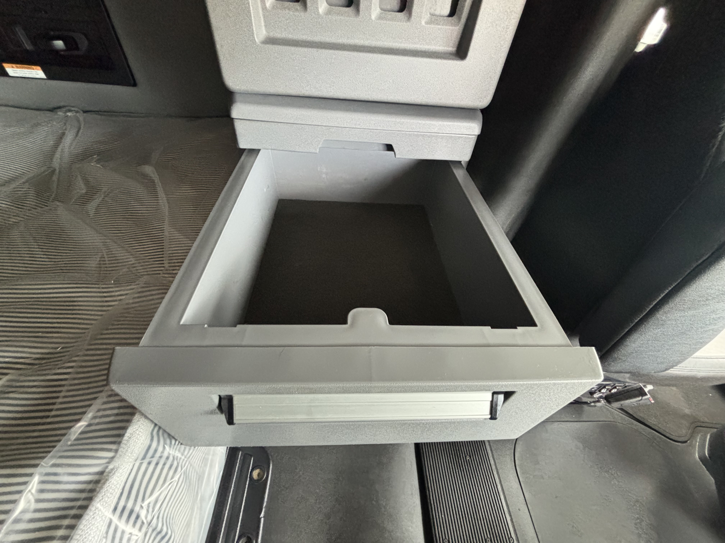Open center console drawer in a Mack AN64T70 cab showing a shallow storage drawer with light gray plastic and surrounding dashboard area.