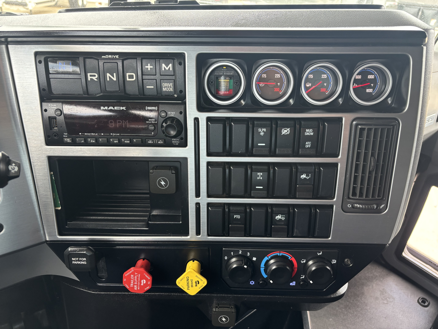 Dash panel of a 2023 Mack AN64T70 showing gauges, radio, climate controls, and various switches.