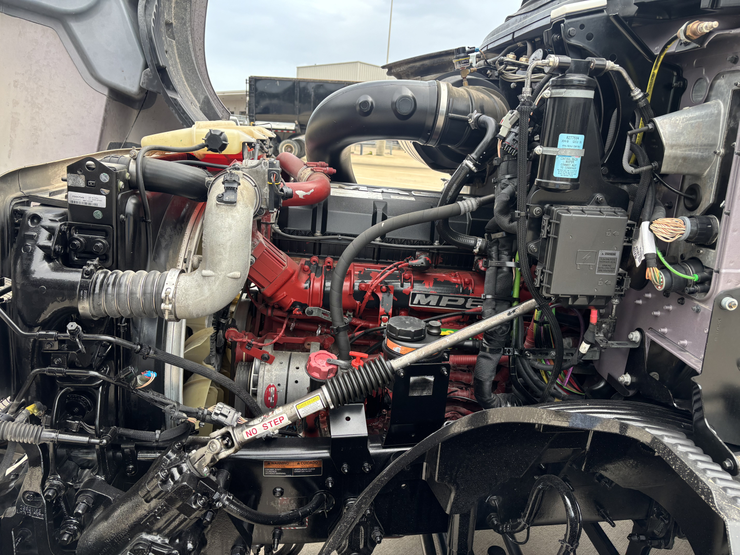 Engine bay of 2023 Mack AN64T70 truck showing red engine, hoses, air intake, and various electrical components.