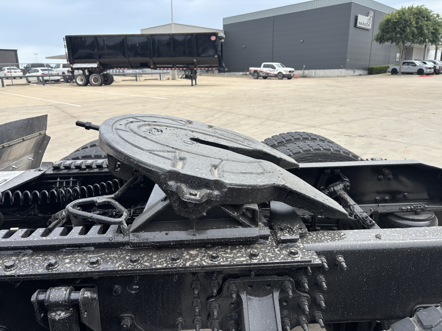 Mechanic's view of a Mack AN64T70 truck chassis with fifth wheel and suspension components in a parking lot.